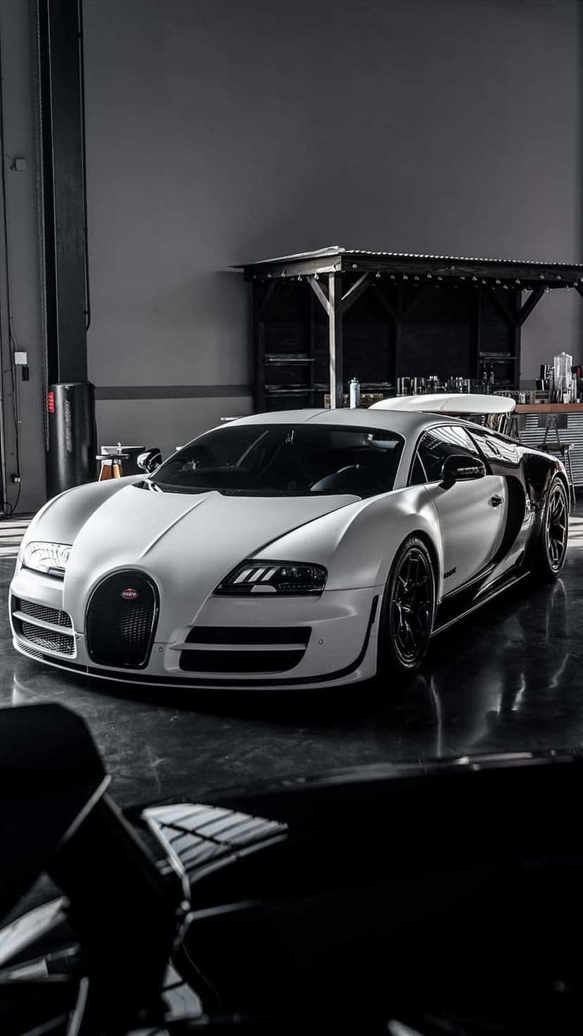 White Bugatti Veyron supercar parked on a reflective garage floor with visible headlights and a matte finish.