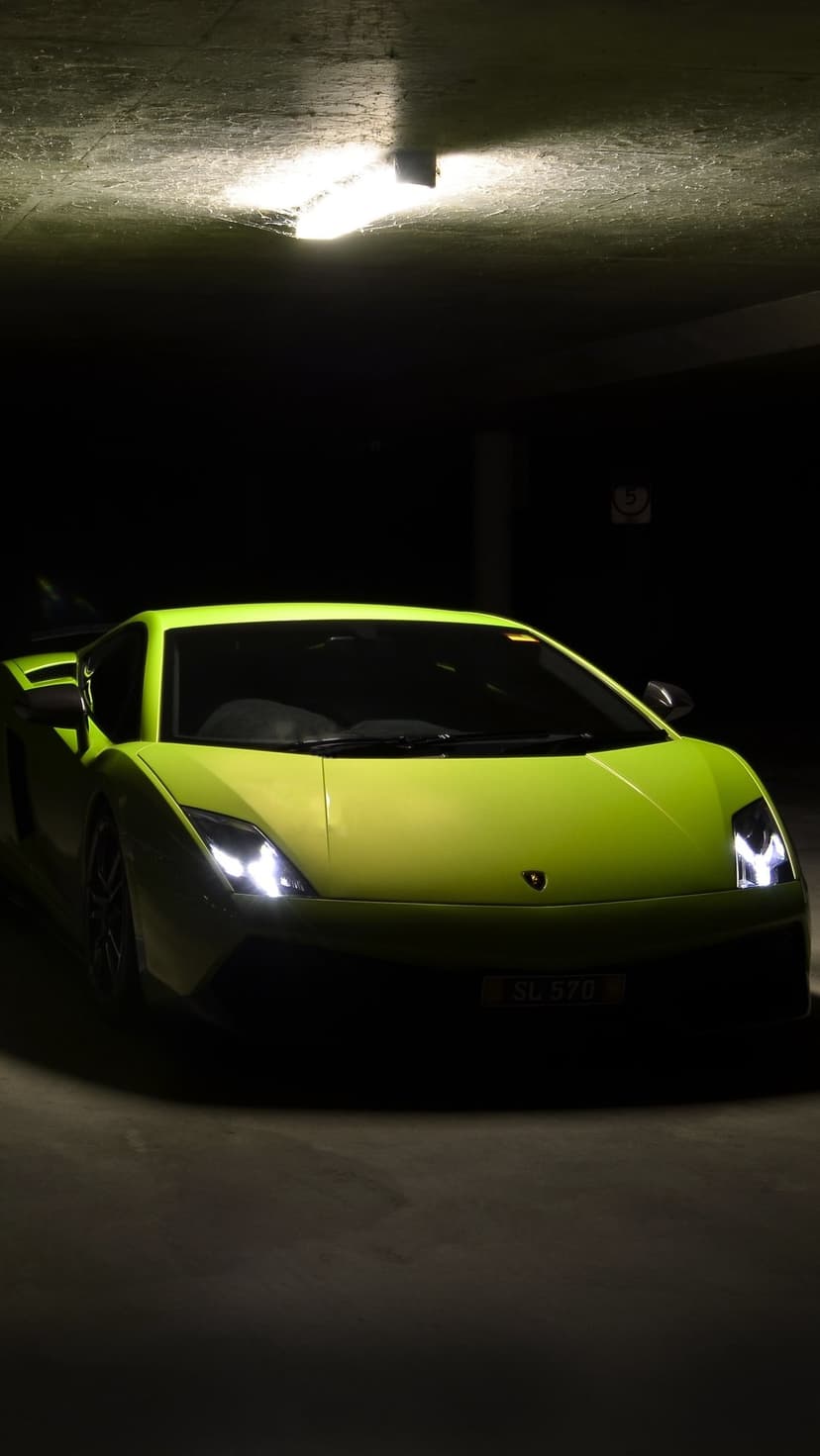 Lime green Lamborghini Gallardo parked in a dark garage with overhead lighting highlighting its sharp body lines.