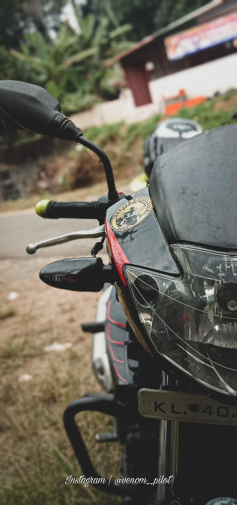Motorcycle headlight assembly with red accents and a biker sticker against a blurred rural road background.