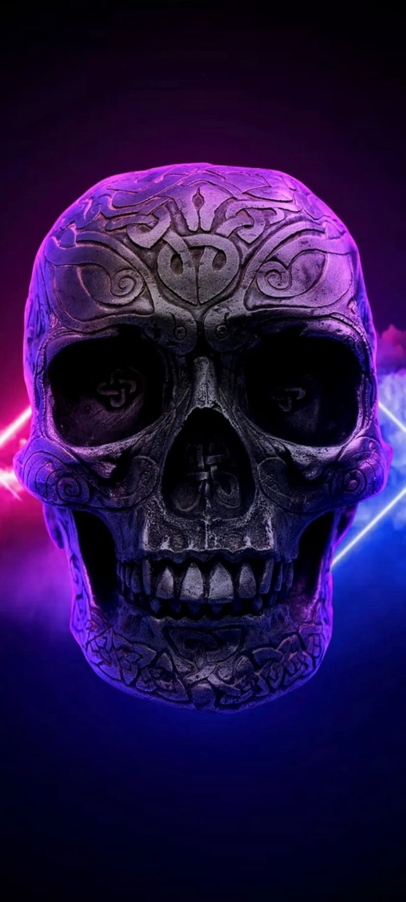 Carved black skull with swirling filigree patterns lit by vibrant neon pink and blue light in a smoky environment.