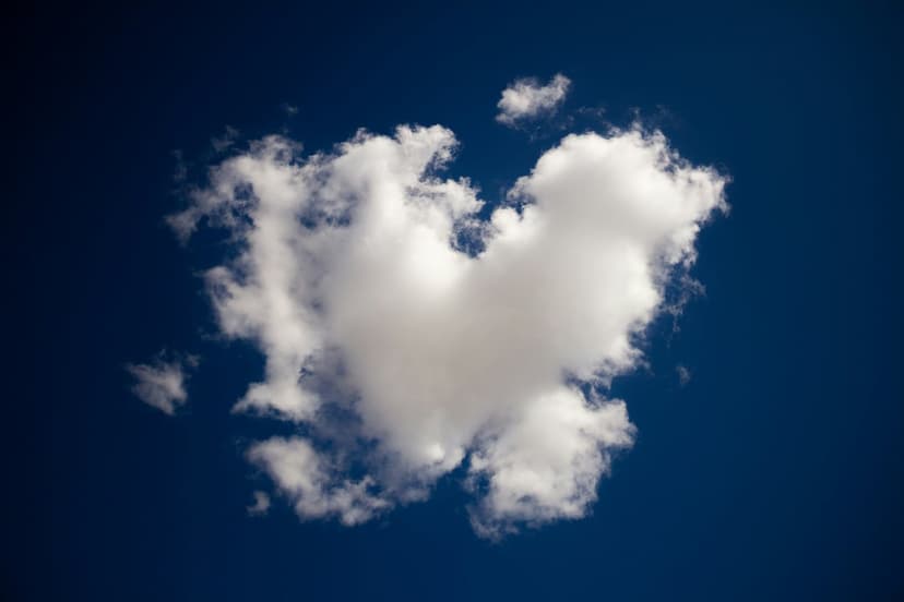 Heart-shaped white cloud floating in a clear blue sky illuminated by bright, direct sunlight in a vertical view.