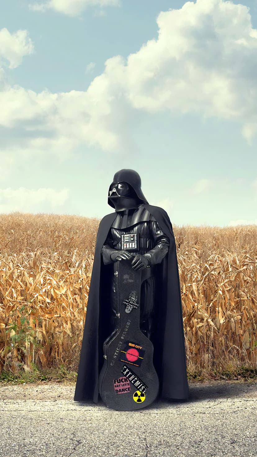 Darth Vader stands in a vast golden wheat field holding a guitar case under a bright, clear blue summer sky.