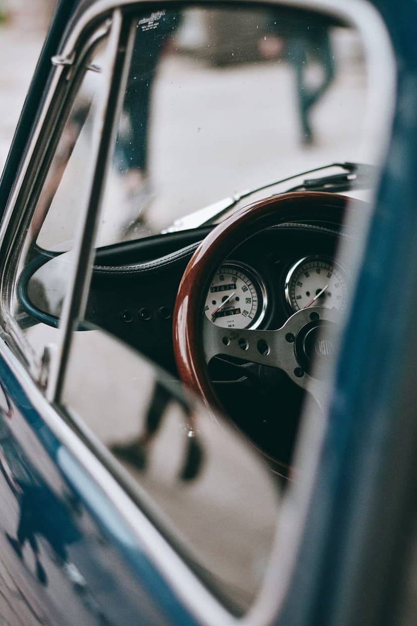 Wood steering wheel and analog gauges of a classic car shown in a vertical close-up with soft reflections.