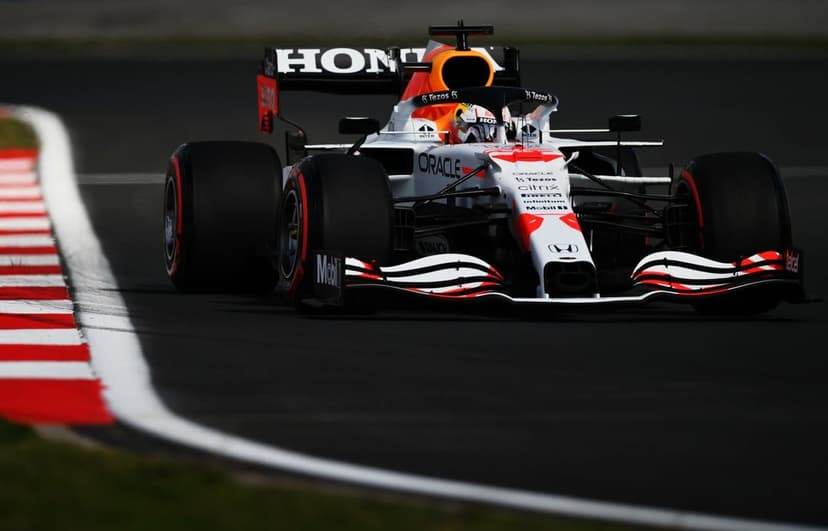 White Red Bull Formula 1 car racing on a dark track with red and white kerbs under intense afternoon sunlight.