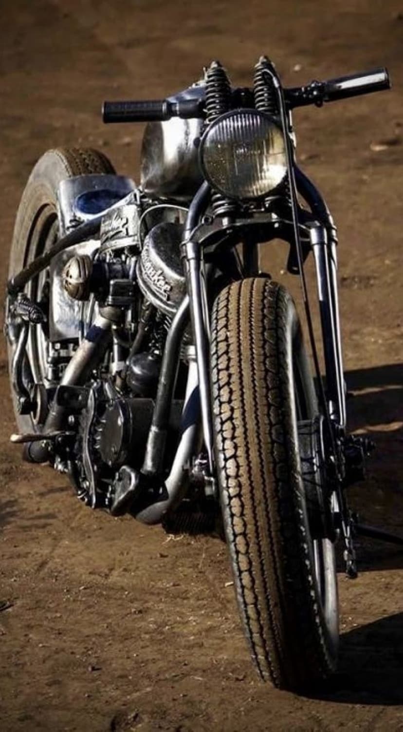 Custom chopper motorcycle featuring a chrome fuel tank, round headlight, and dual springs in a dusty setting.
