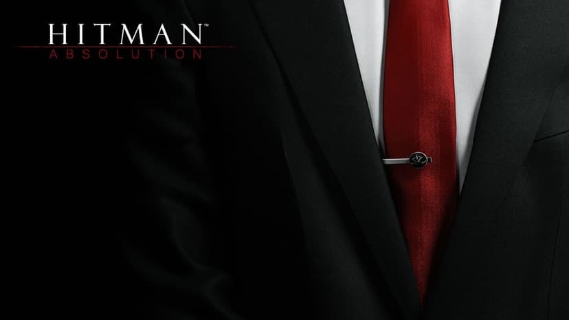 Close-up of a man in a black suit, white shirt, and red tie with a silver clip against a dark background.