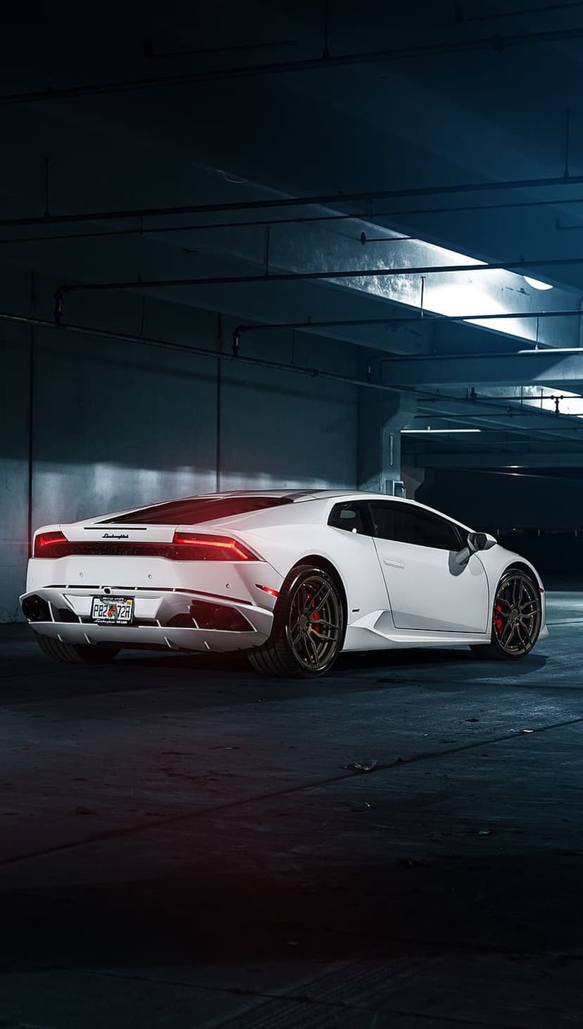 White Lamborghini Huracan with glowing red taillights parked in a dark garage with moody metallic reflections.