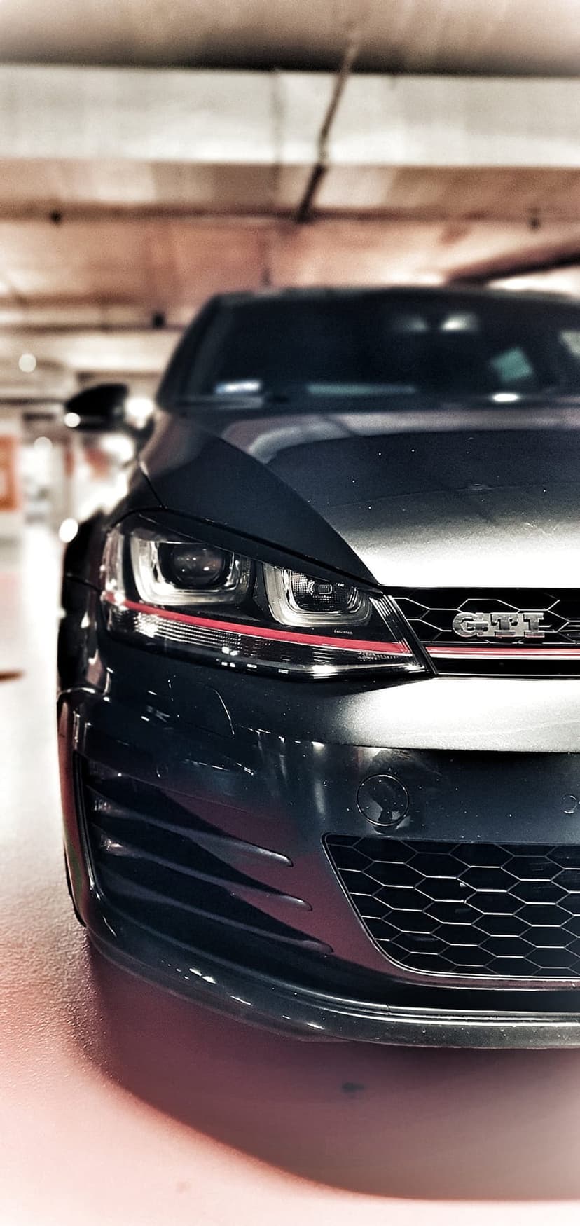 Dark grey Volkswagen Golf GTI front grille and headlights with red trim in a low-angle garage close-up.