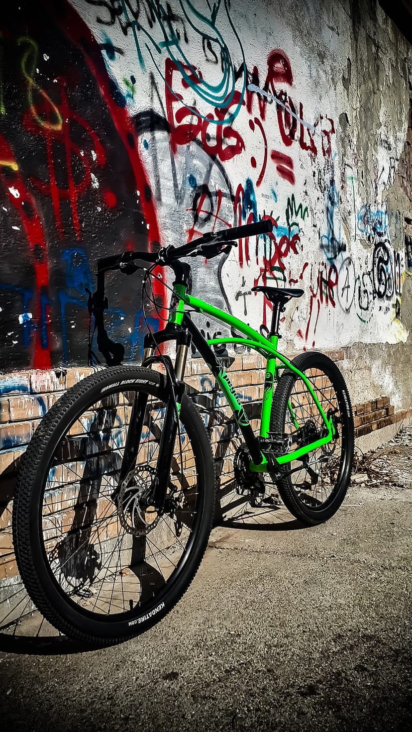 Green mountain bike with detailed spokes parked in front of a colorful, multi-layered graffiti street art wall.
