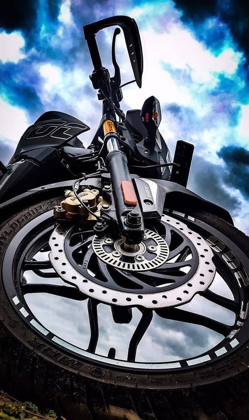 Black motorcycle front wheel and disc brake seen from a low angle against an overcast sky with high handlebars.
