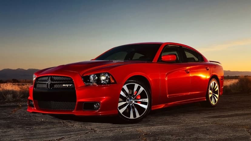 Red muscle car with a black grille and silver wheels parked on a flat road during a golden hour sunset.