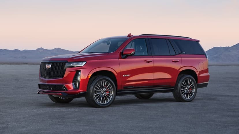 Red Cadillac Escalade-V parked on a vast desert floor under a soft pink sunset sky with distant mountains.