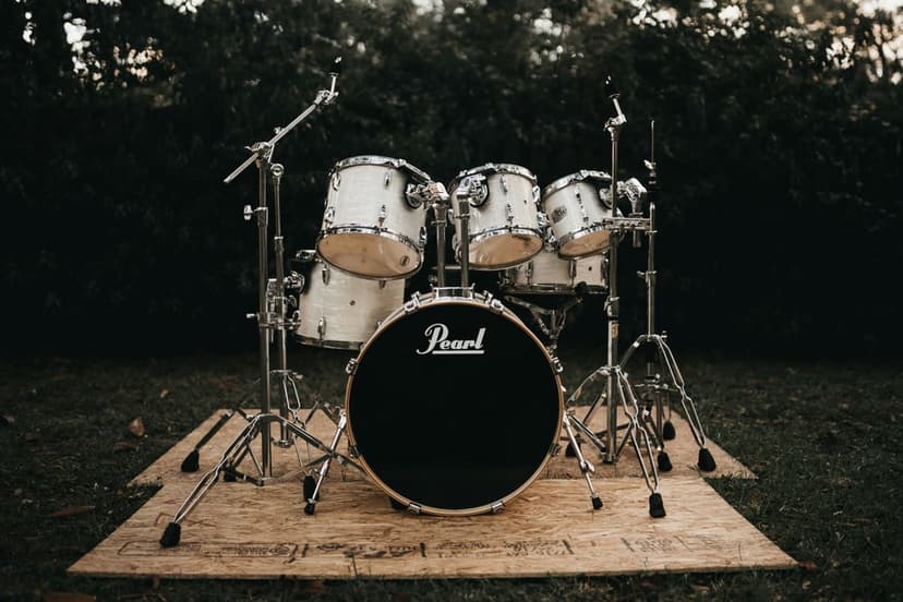 White Pearl drum set on a wooden deck surrounded by green grass and dense dark foliage in natural light.