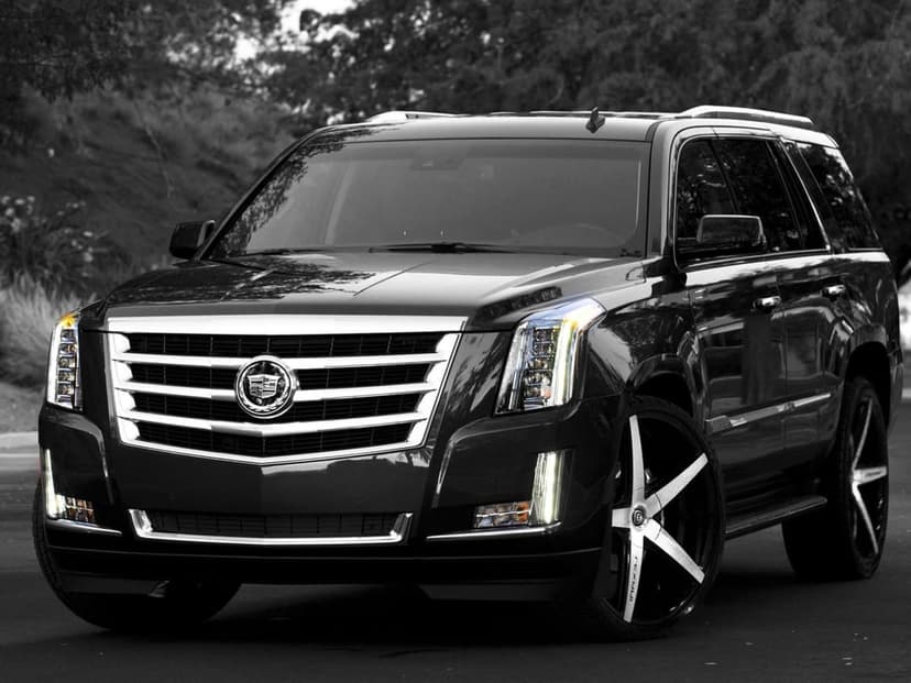 Front view of a black Cadillac Escalade SUV featuring a chrome grille and large custom wheels on a paved road.