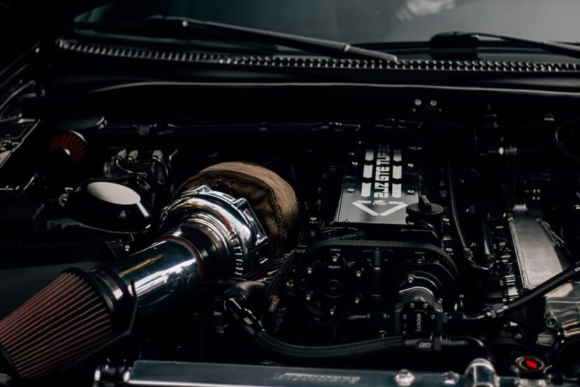 Chrome turbocharger with heat-wrapped piping and a red intake filter inside a dark modified car engine bay.