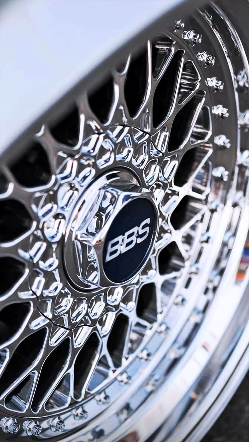 Polished chrome BBS mesh wheel hub featuring a central logo and intricate silver spokes with light reflections.