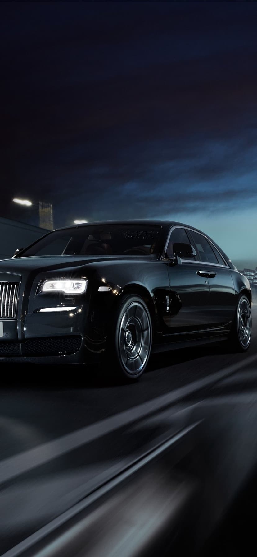Black Rolls-Royce sedan driving on a dark highway at night with glowing LED headlights and motion blur.