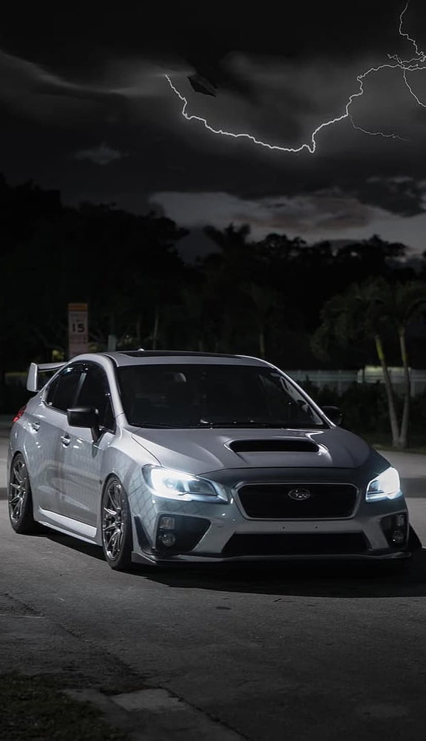 Silver Subaru WRX STI parked on a dark street while bright lightning strikes through heavy storm clouds above.