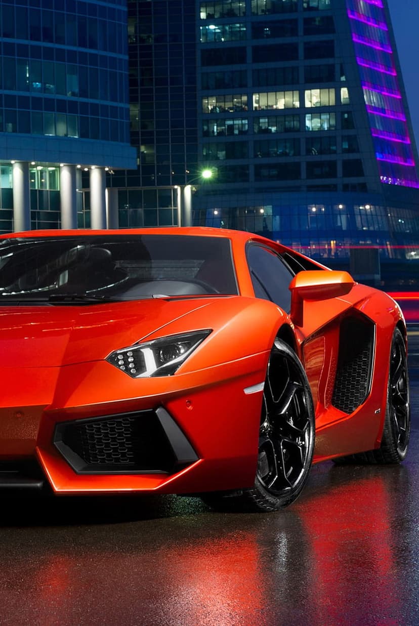 Orange Lamborghini Aventador parked on a wet city street at night reflecting bright skyscraper lights nearby.