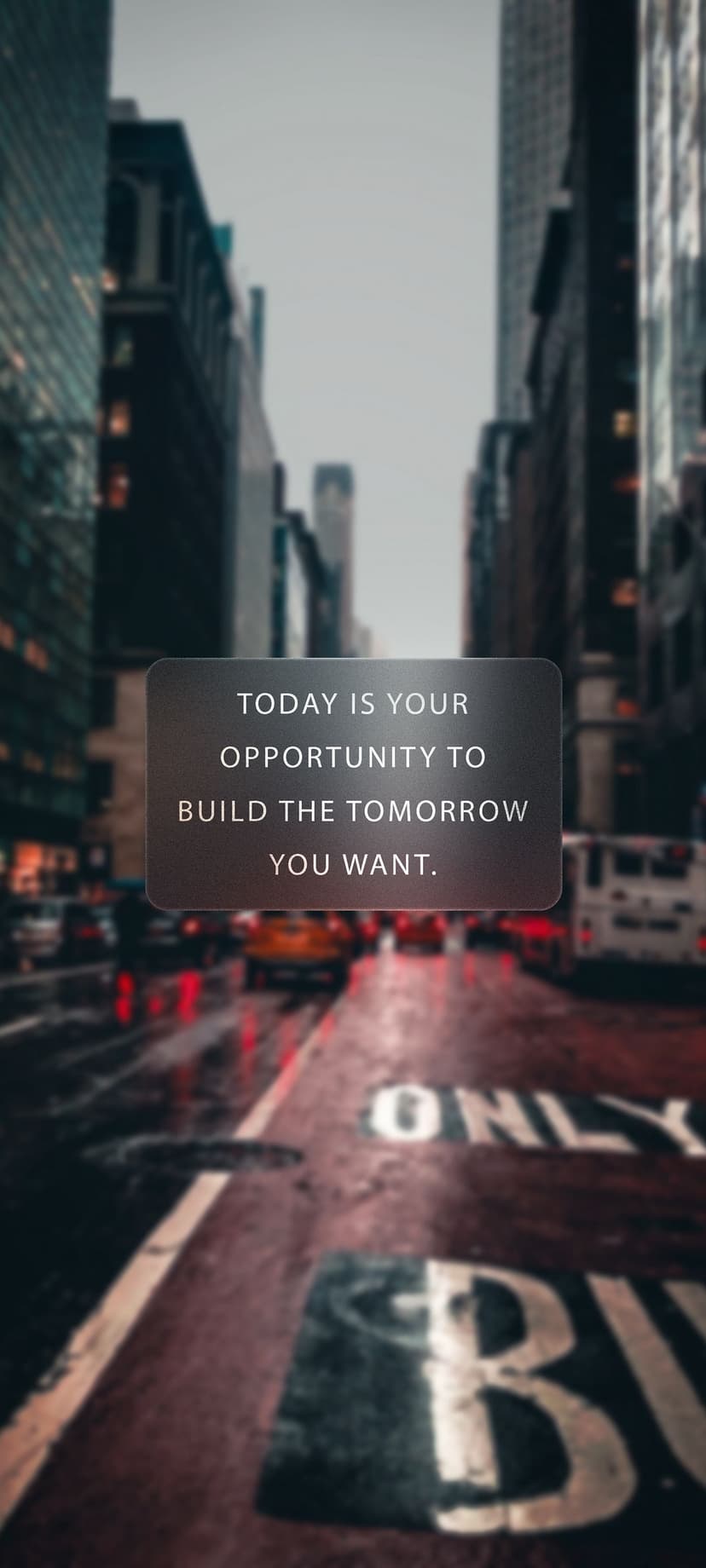 Motivational text overlays a blurred evening city street with glowing red traffic lights and rain-slicked asphalt.