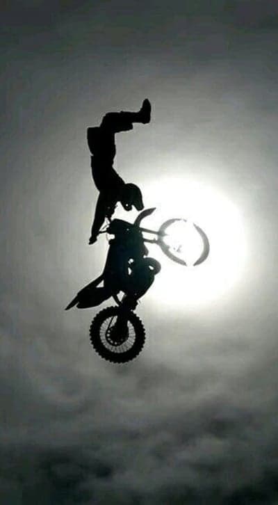 Motocross Stunt Silhouette Phone Wallpaper under Sunlit Sky