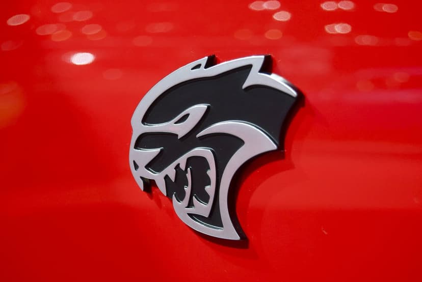 Silver Dodge Hellcat emblem with black accents centered on a vibrant glossy red car surface with soft bokeh.