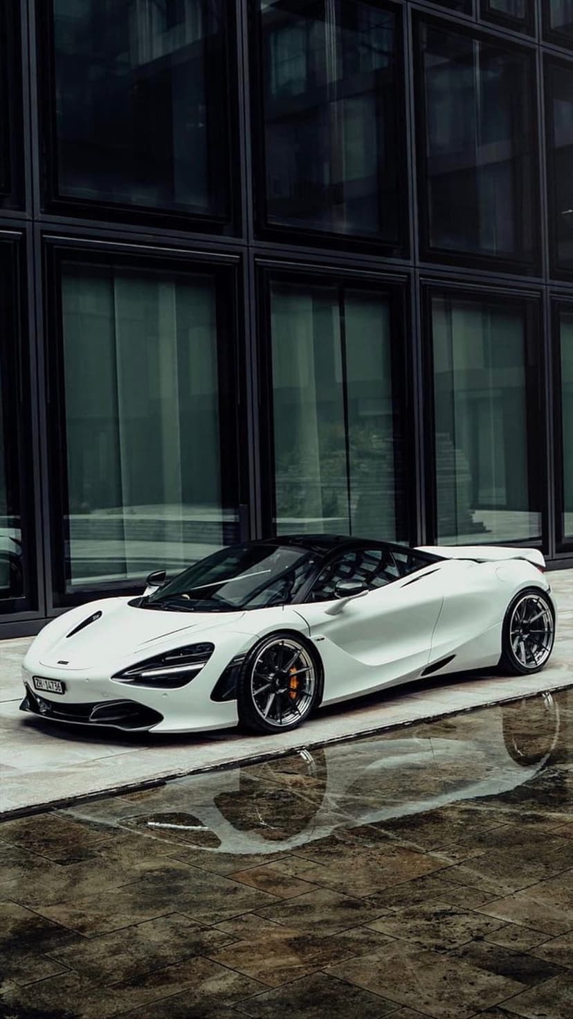 White McLaren 720S parked on wet pavement in front of a modern glass building with dark reflective windows.