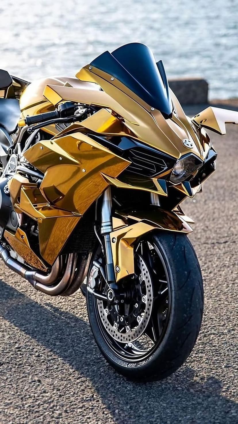 Gold Kawasaki Ninja H2R motorcycle with reflective chrome fairings parked on asphalt near a blurred ocean background.