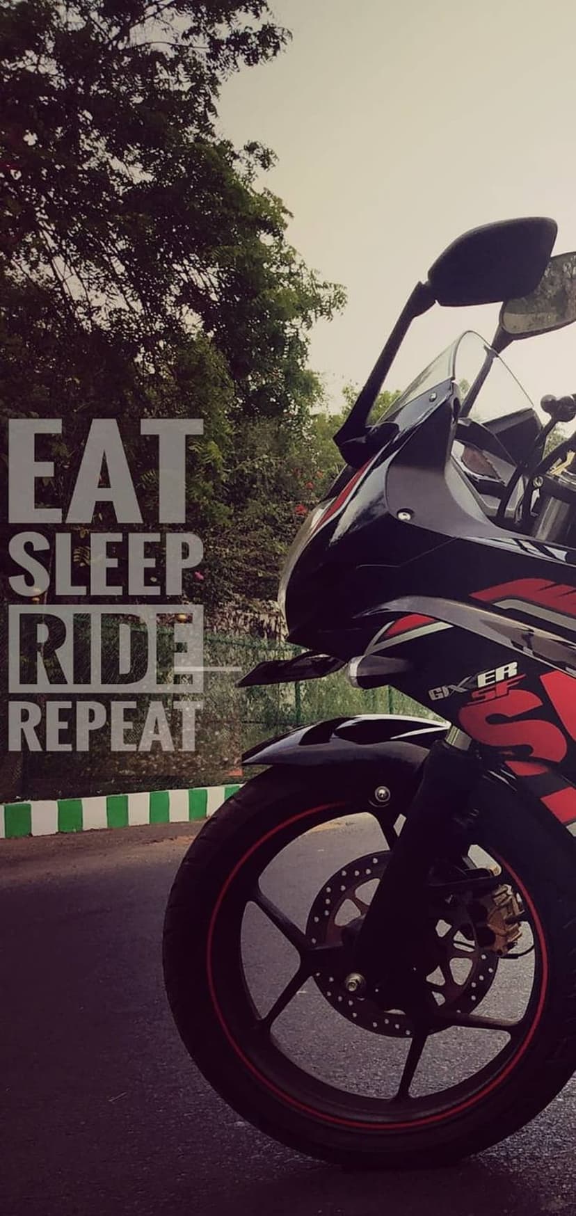 Sporty black and red motorcycle parked on a road with Eat Sleep Ride Repeat text and green forest background.