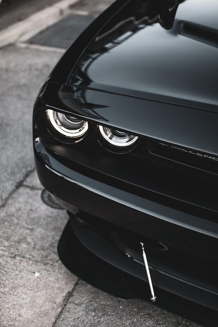 Dodge Challenger dual headlights glow against polished black bodywork with a detailed honeycomb grille visible.