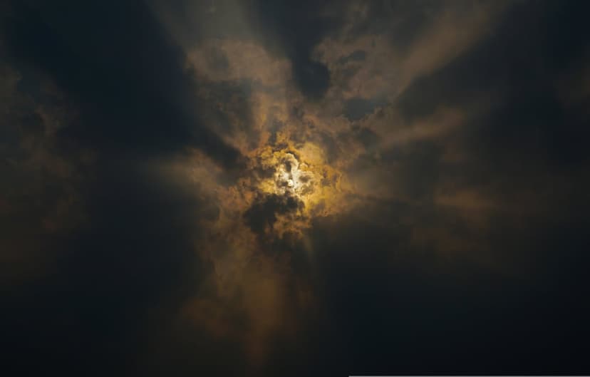 Golden sunbeams pierce through heavy dark storm clouds in a high-contrast, dramatic sky composition.