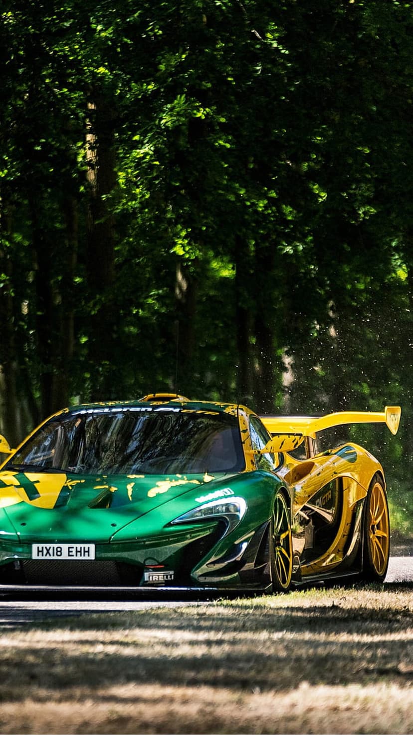 McLaren P1 hypercar in green and yellow racing livery speeds along a forest road with visible motion blur.