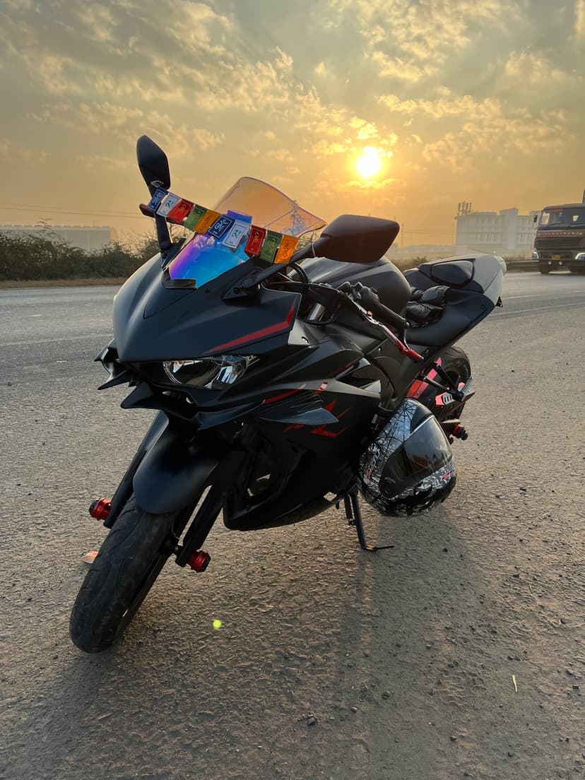 Black sportbike with prayer flags and a helmet sits roadside under a glowing golden hour sunset.