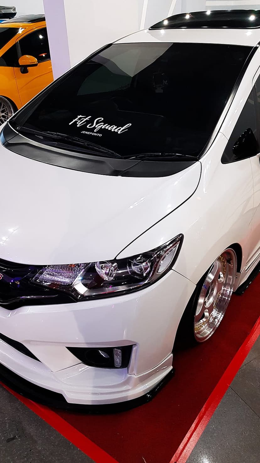 White Honda Jazz featuring a slammed stance, custom body kit, and chrome wheels with a Fit Squad decal.