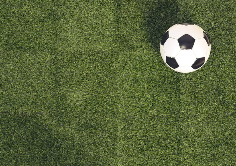 Soccer ball centered on synthetic green turf from an overhead view, showcasing textured grass and leather panels.