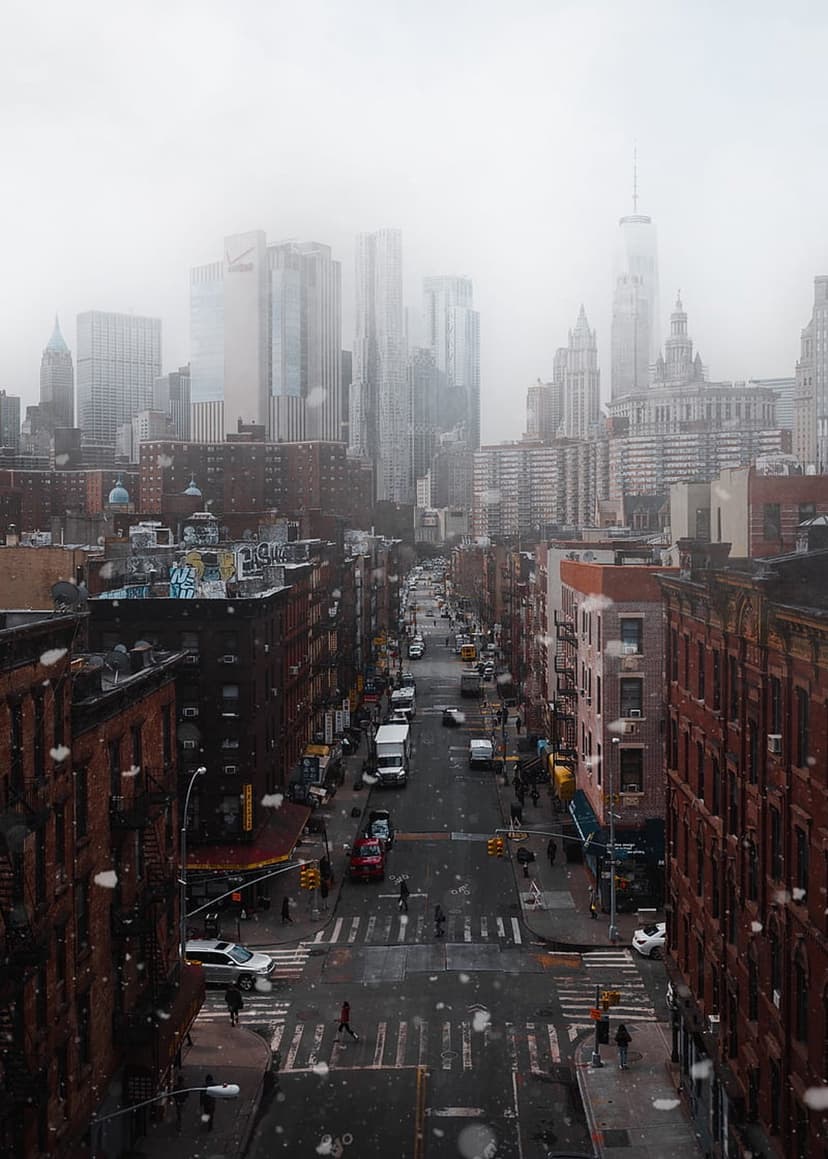 Misty Manhattan street view from above featuring historic brick buildings and foggy skyscraper silhouettes.