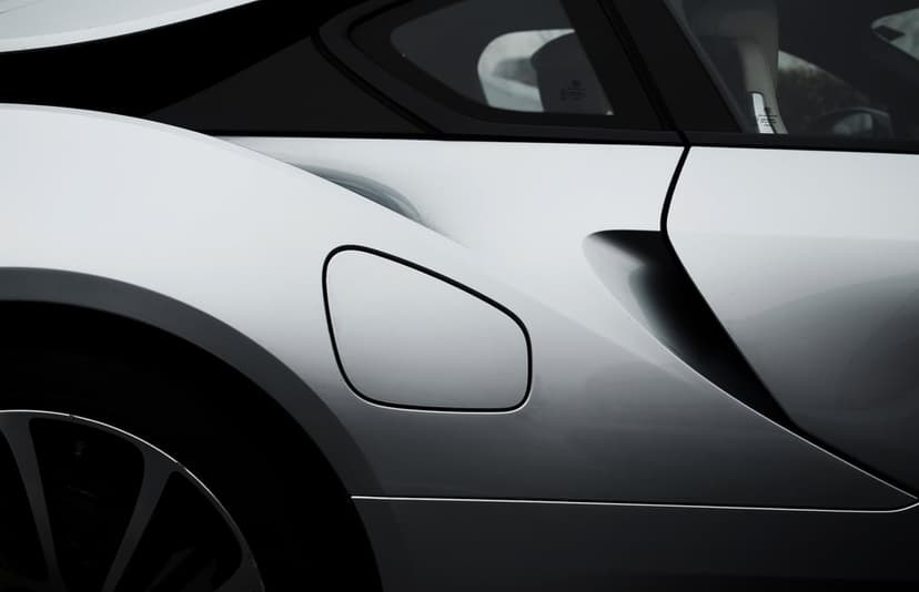 Silver sports car fuel door and aerodynamic rear panel with reflective metallic paint and sharp body lines.