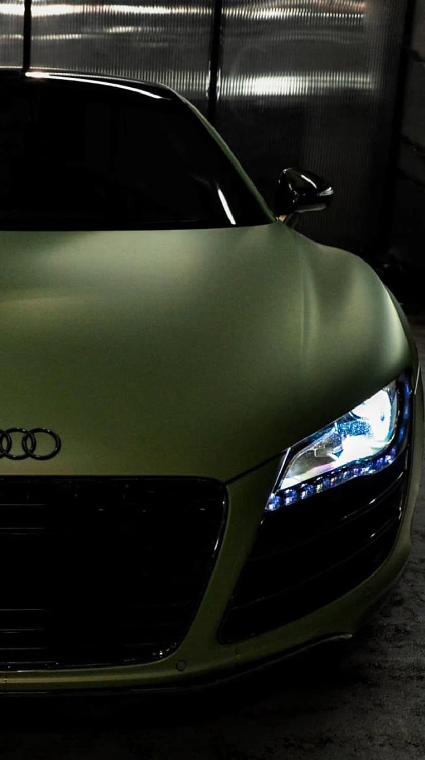 Matte green Audi R8 front end with glowing LED headlights and dark grille in a close-up automotive portrait.