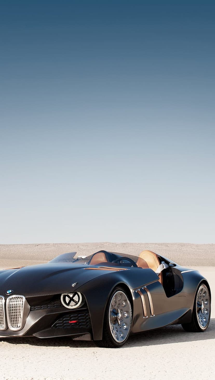Dark BMW concept car with tan interior parked on desert sand under a clear blue sky during daylight.
