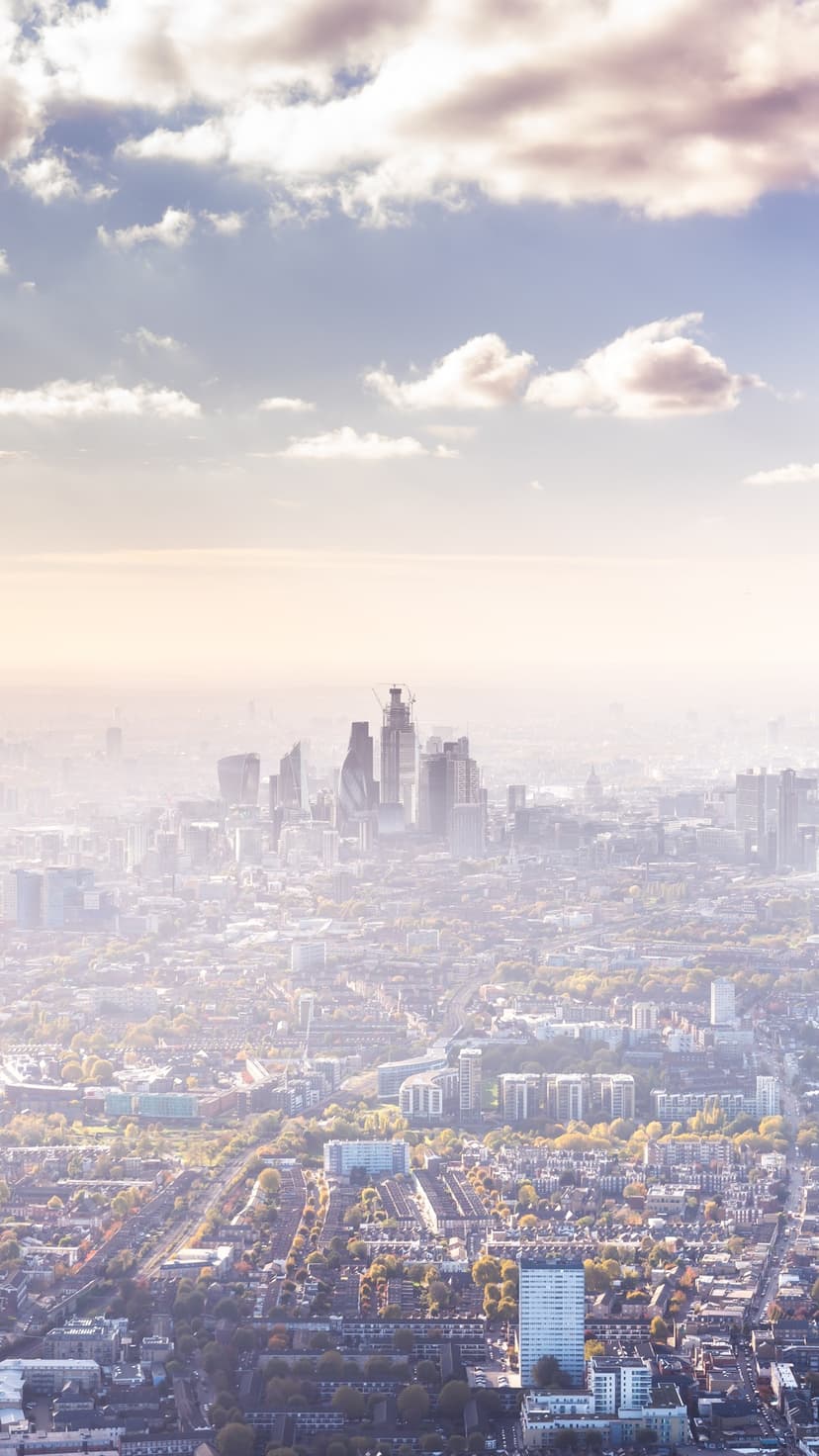 London skyscrapers rise through a thick layer of morning haze above a sprawling grid of residential streets.