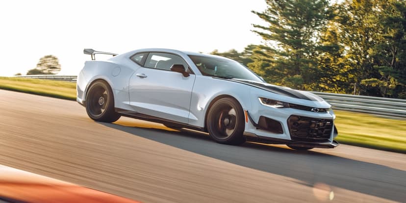 White Chevrolet Camaro ZL1 1LE racing on a track with motion blur and warm golden hour sunlight during sunset.