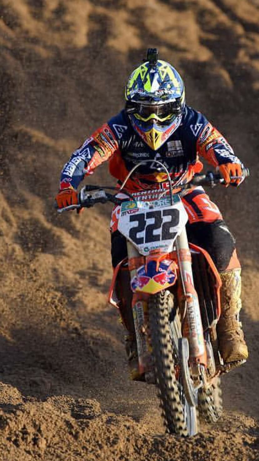 Motocross rider number 222 kicks up sand on a dirt track in vibrant orange and blue gear on a racing bike.