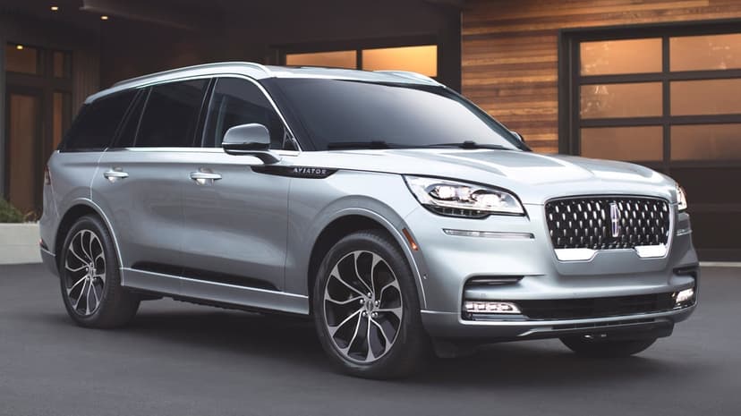 Silver Lincoln Aviator SUV parked on a dark driveway in front of a modern wood and glass house at sunset.