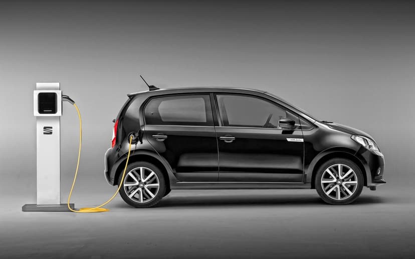 Black Seat Mii Electric car connected to a white charging station with a yellow cable in a studio.