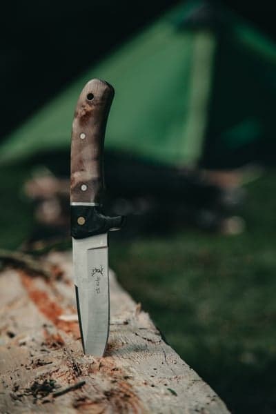 Hunting Knife Stuck in Log, Camping Tent Background