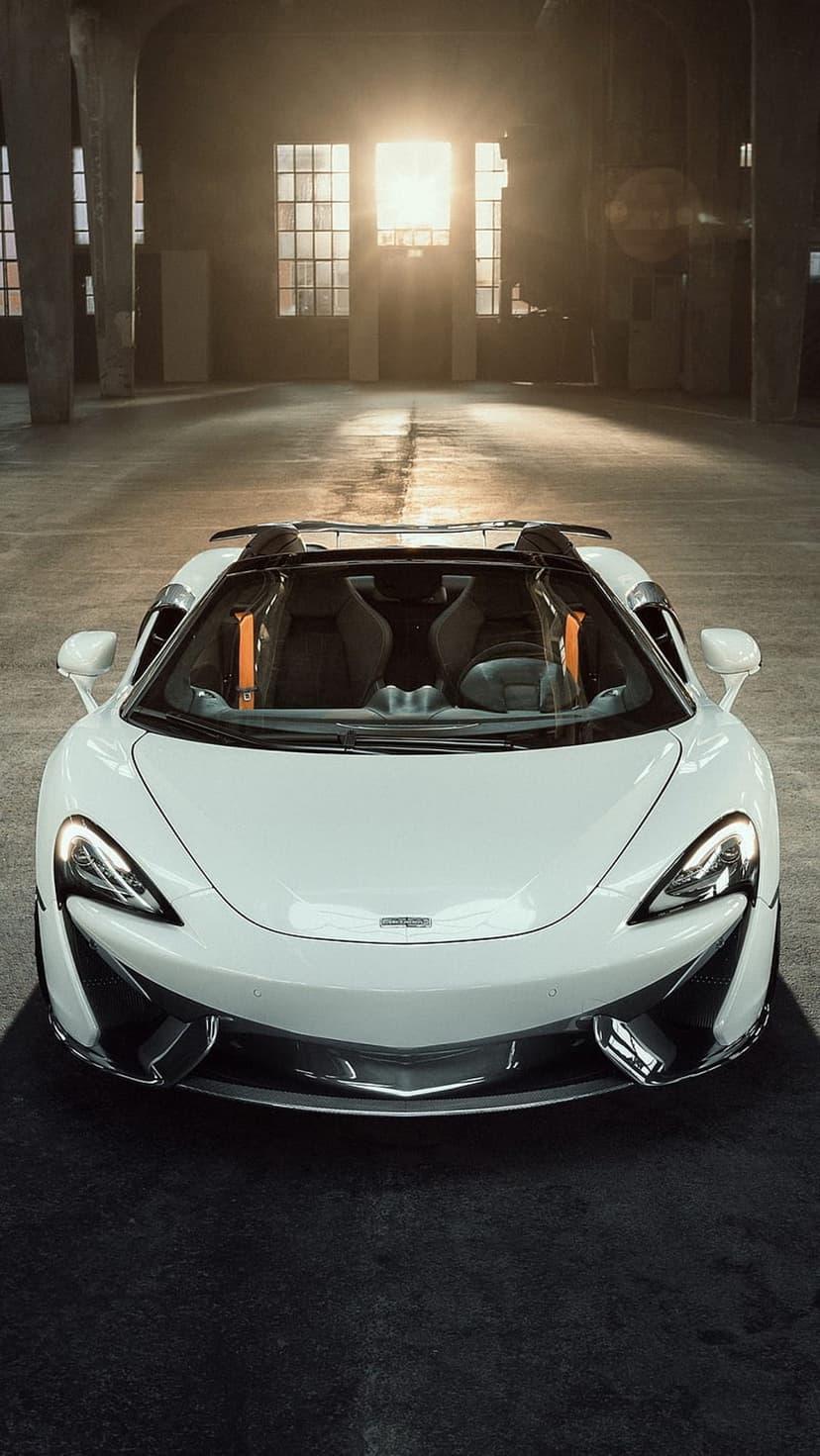 White McLaren convertible parked in a sunlit industrial warehouse with dramatic light through windows.