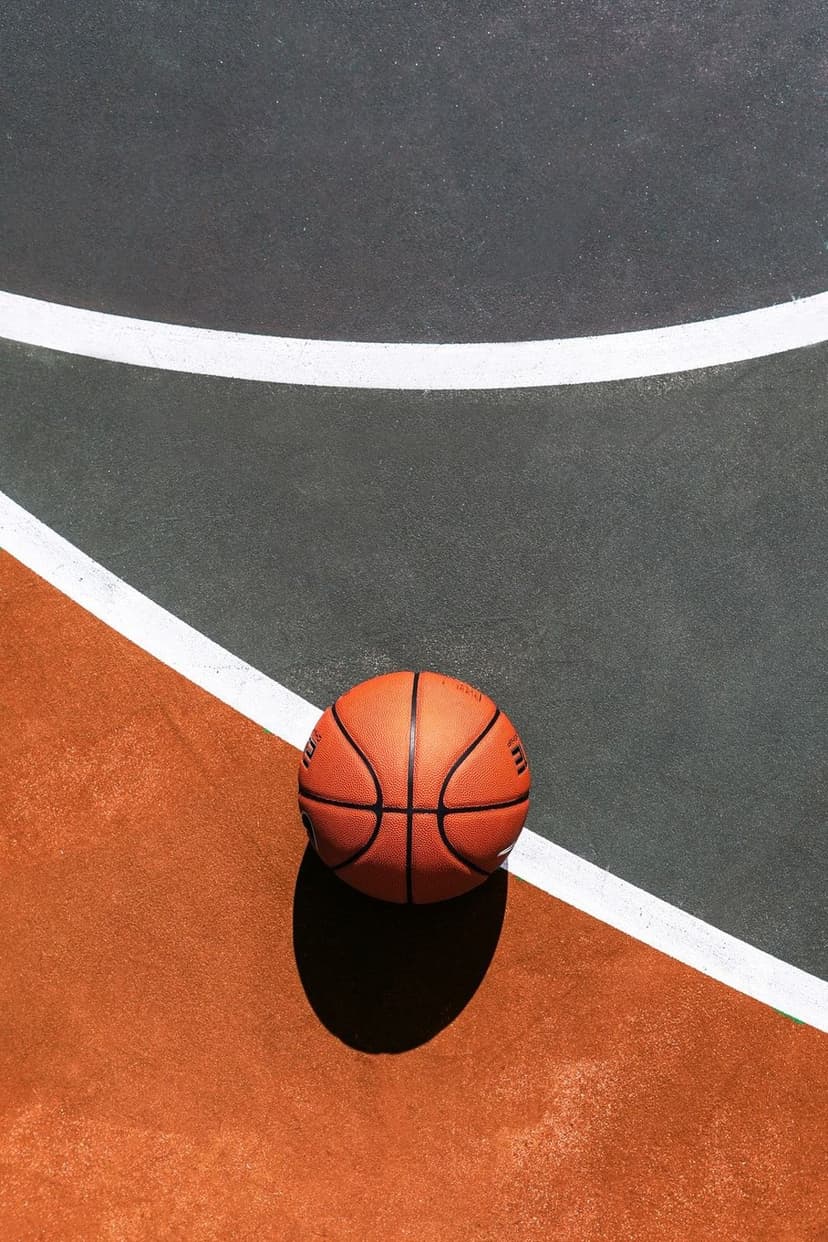 Orange basketball resting on a white painted boundary line of a grey and brown textured outdoor athletic court.
