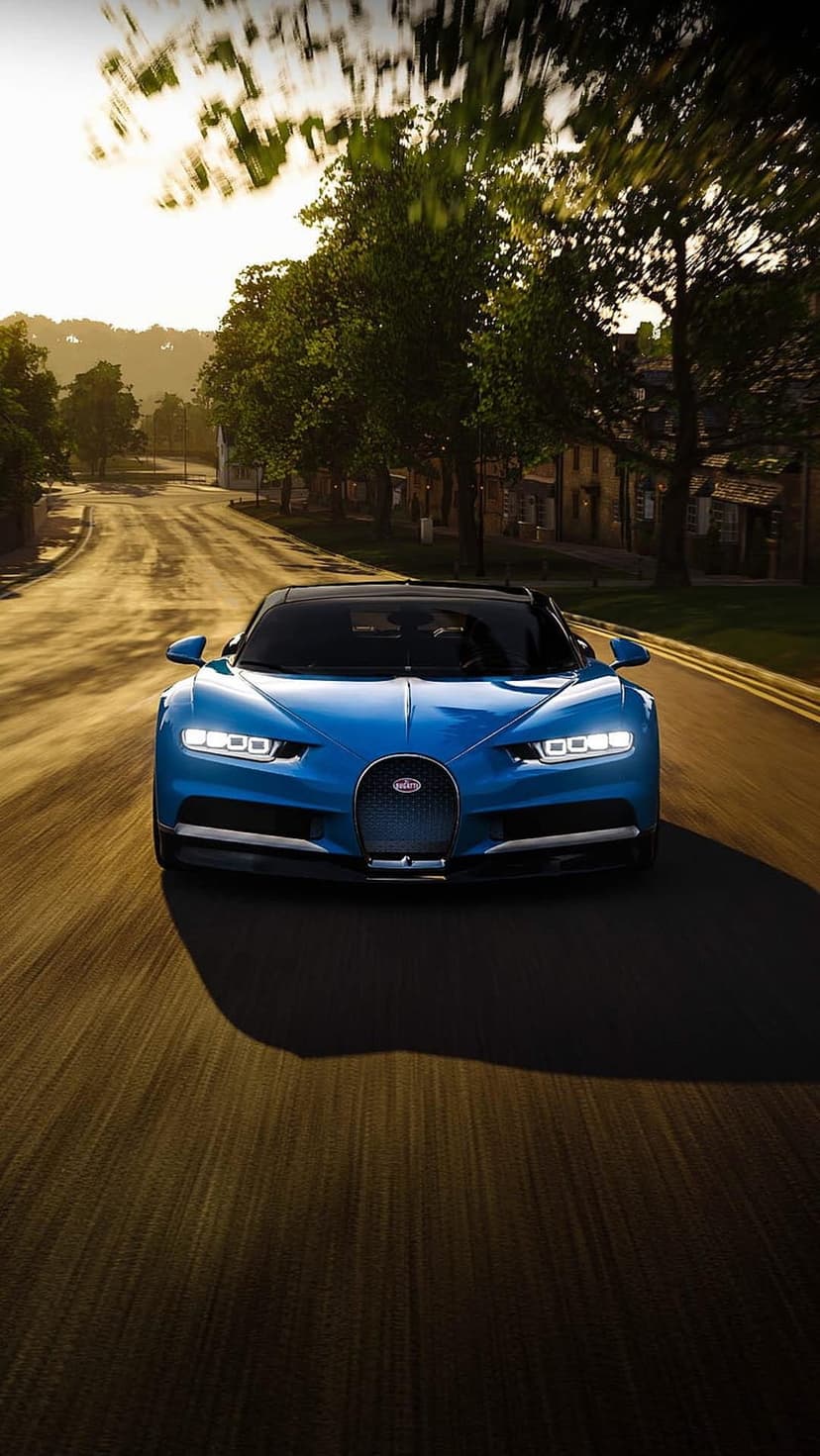 Bugatti Chiron in blue driving on a sun-drenched road past green trees and buildings during golden hour sunset.
