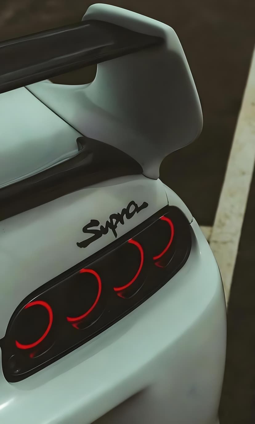 Toyota Supra rear view featuring four glowing red circular taillights, a white spoiler, and metallic badging.