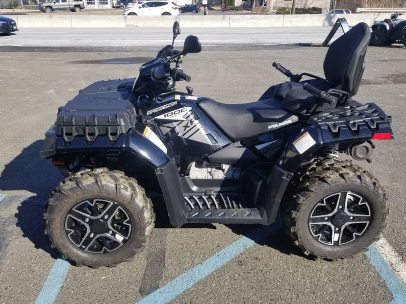 Black Polaris Sportsman 1000 XP ATV with off-road tires parked on asphalt under bright sunlight.